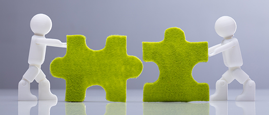 Symbolbild: Zwei kleine, weiße Figuren schieben zwei übergroße Puzzleteile aufeinander zu