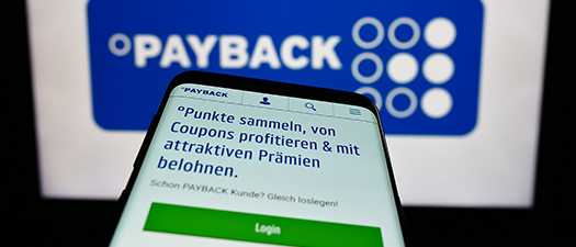 Symbolbild: Nahaufnahme eines Smartphones, auf dem die Payback-App geöffnet ist. Im Hintergrund ist groß das Payback-Logo zu sehen.