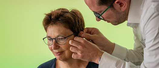 Bildbeschreibung:Hörakustiker passt Hörgerät am Ohr einer Frau an