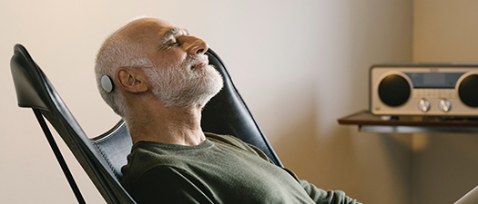 Bildbeschreibung: Mann mit CI liegt im Sessel, hat die Augen zu und genießt. Im Hintergrund sieht man ein Radio.