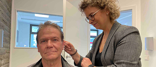 Bildbeschreibung: Die Gründerin Sabine Hönighausen passt in Fachgeschäft „Hörakustik Hönighausen“ einem männlichen Kunden sein Hörgerät an.