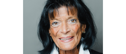Bildbeschreibung: Porträtfoto von Marianne Frickel, auf dem sie lächelnd in die Kamera blickt. Sie ist 71 Jahre alt, trägt halblange schwarze Haare, eine weiße Bluse und einen schwarzen Blazer.